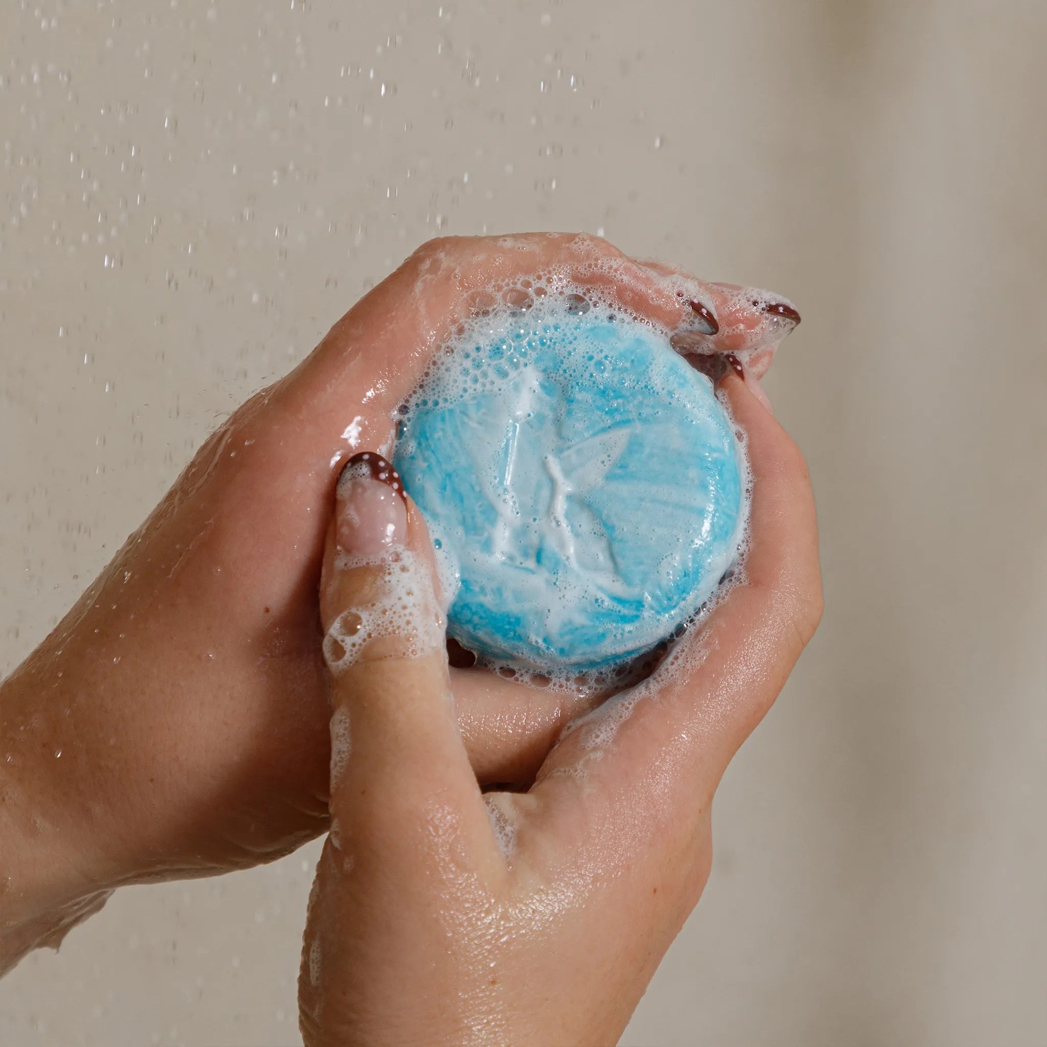 Hand holding a sudsy seaweed shampoo bar against a neutral background