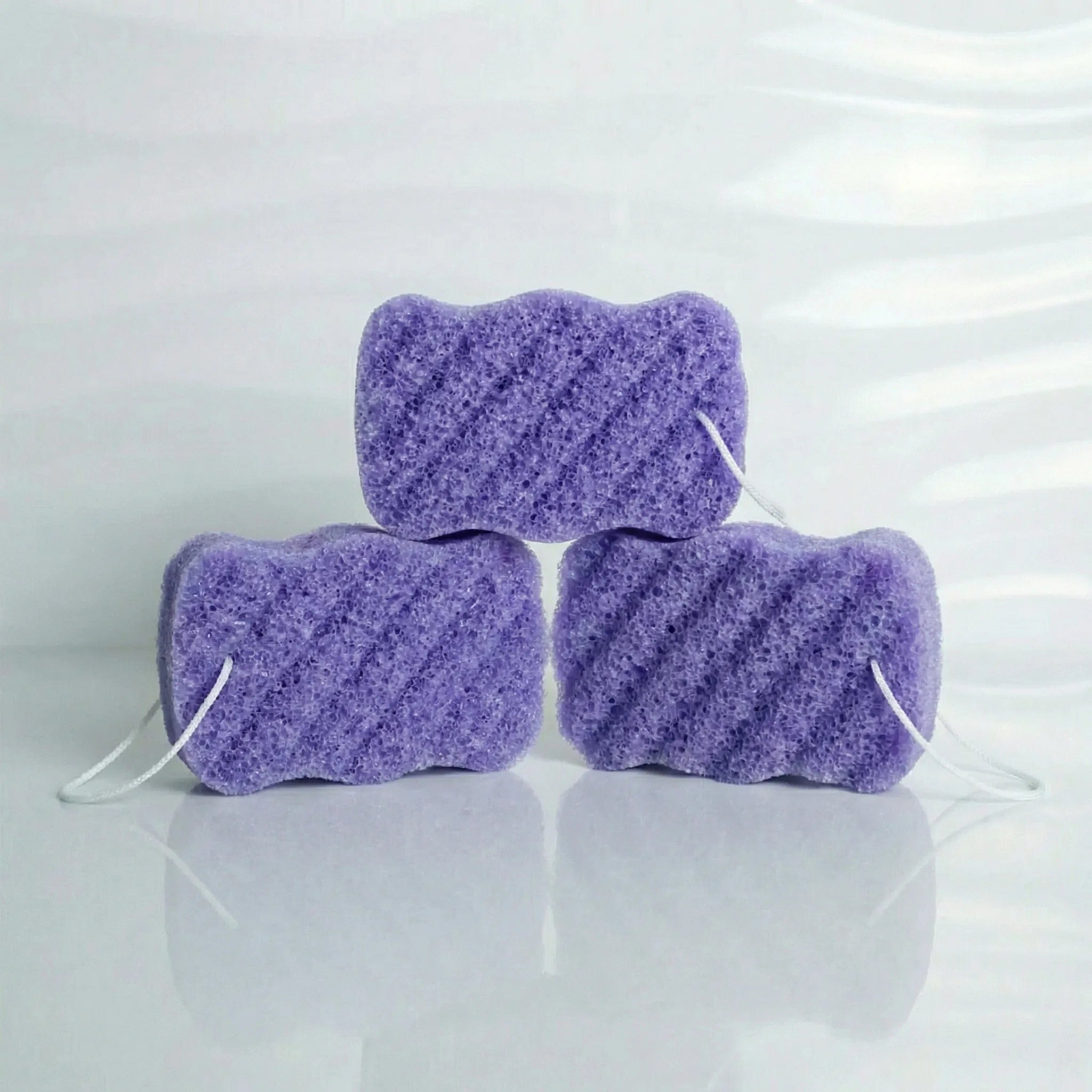 Three lavender konjac body sponges stacked on a white background
