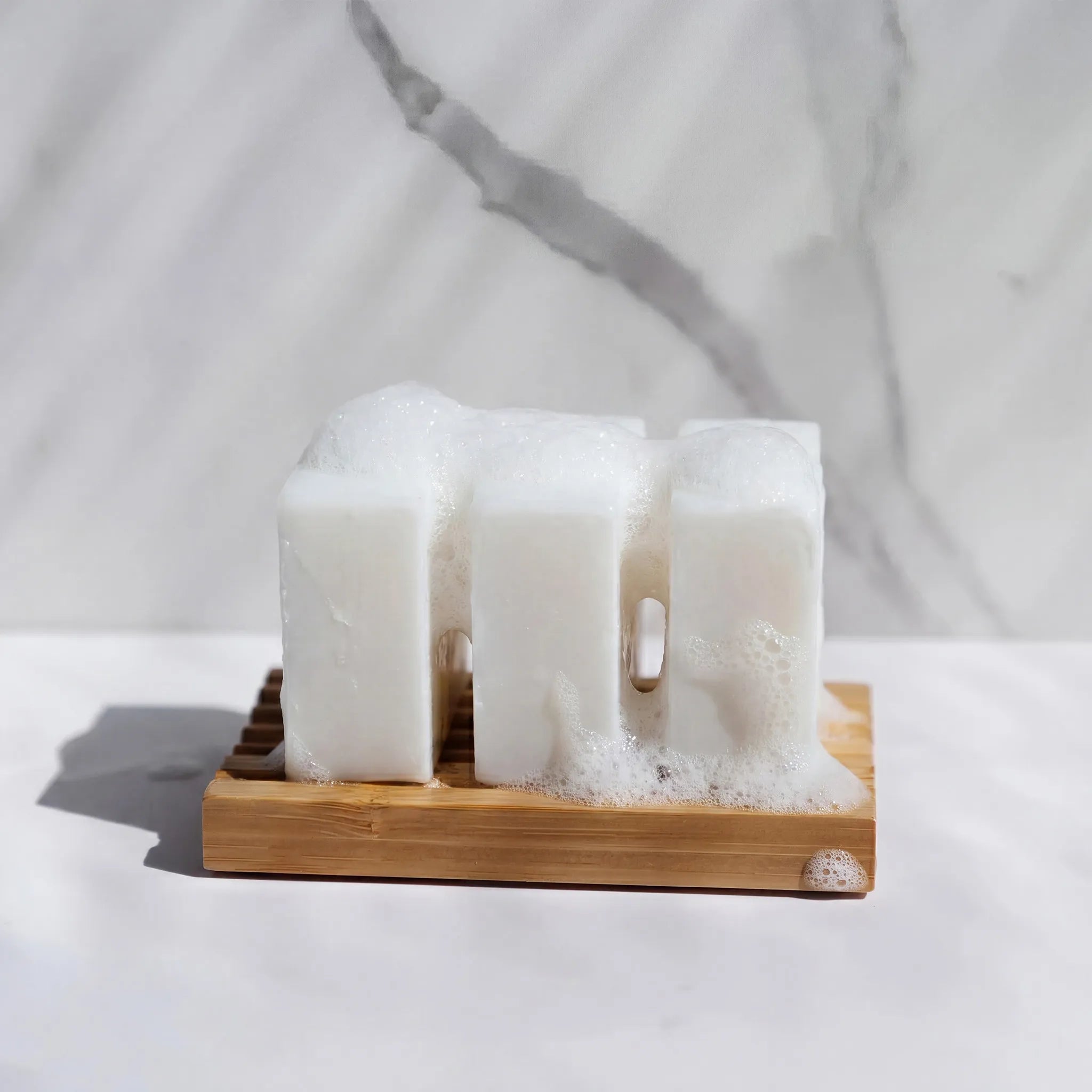 Three stacked dish soap bars on a wooden soap dish against a marble background