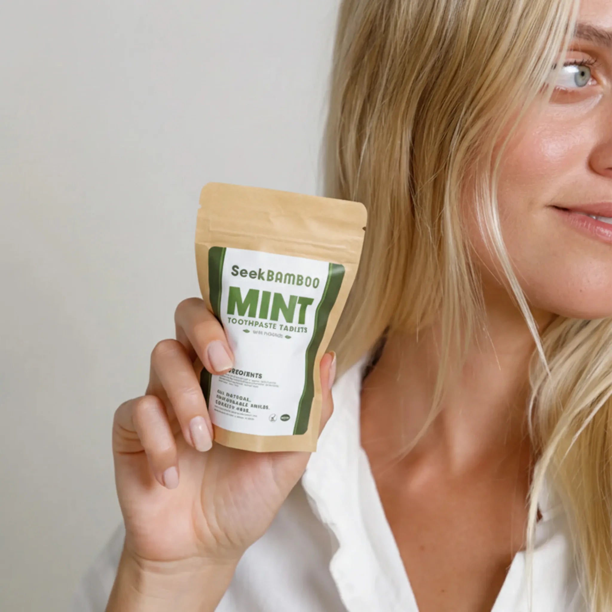 Woman holding a package of Seek Bamboo Mint toothpaste tablets against a plain background
