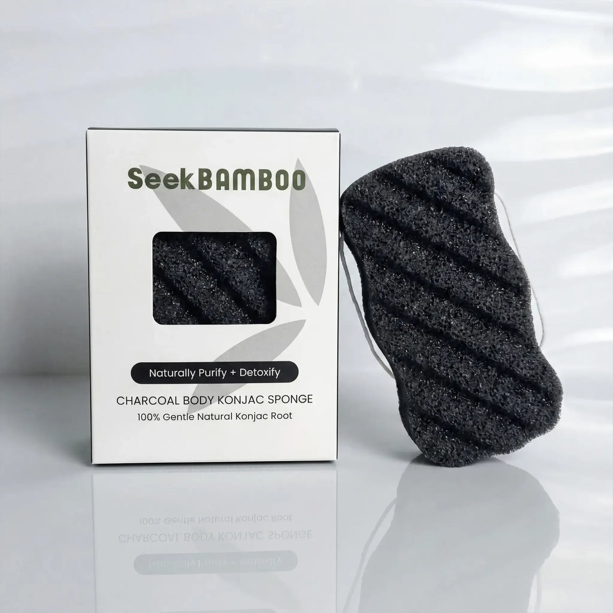 Seek Bamboo charcoal body konjac sponge next to its white packaging box on a reflective white surface.