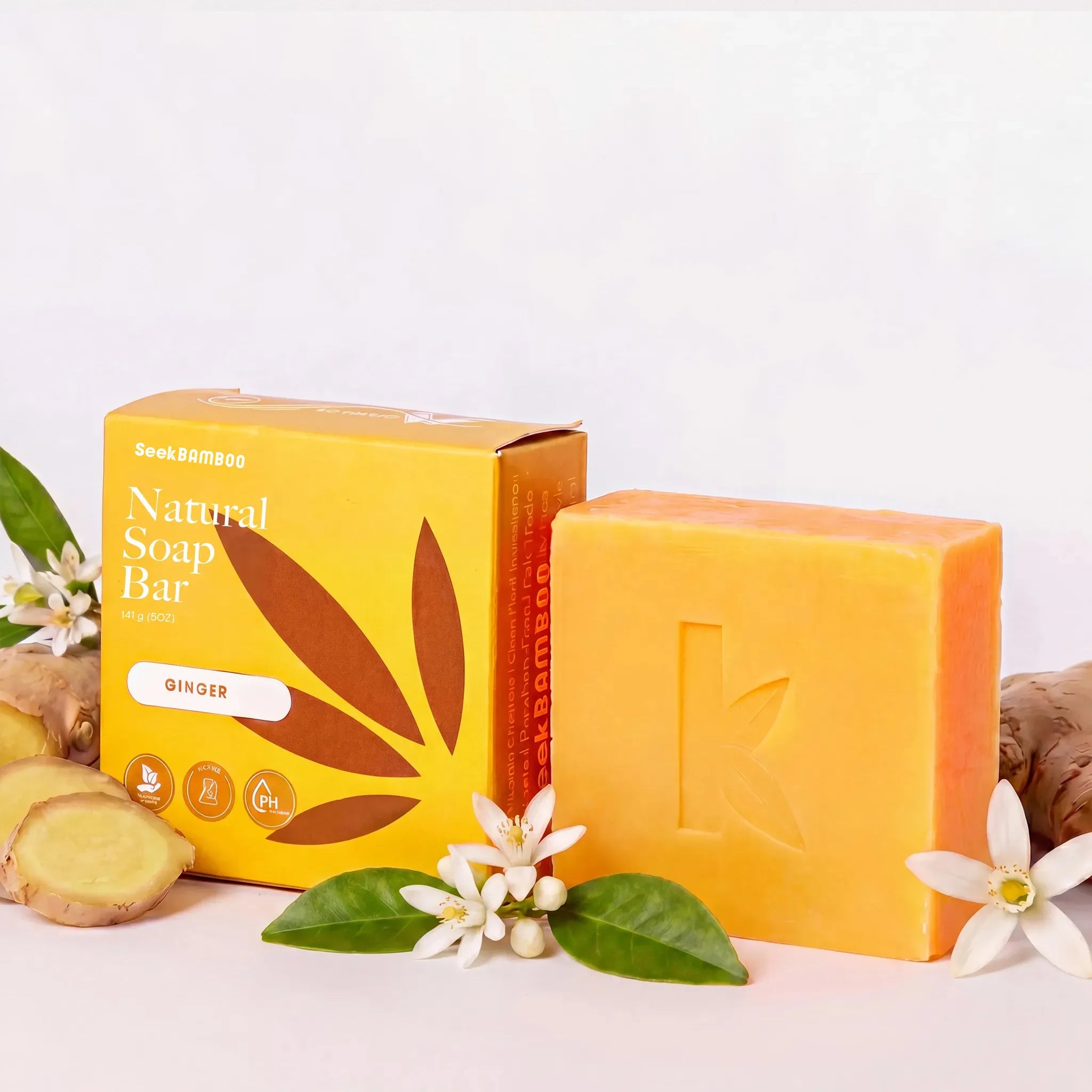 A bar of natural brightening soap bar in ginger scent shown next to its yellow packaging box, styled with ginger roots, white flowers, and green leaves on a clean white background.