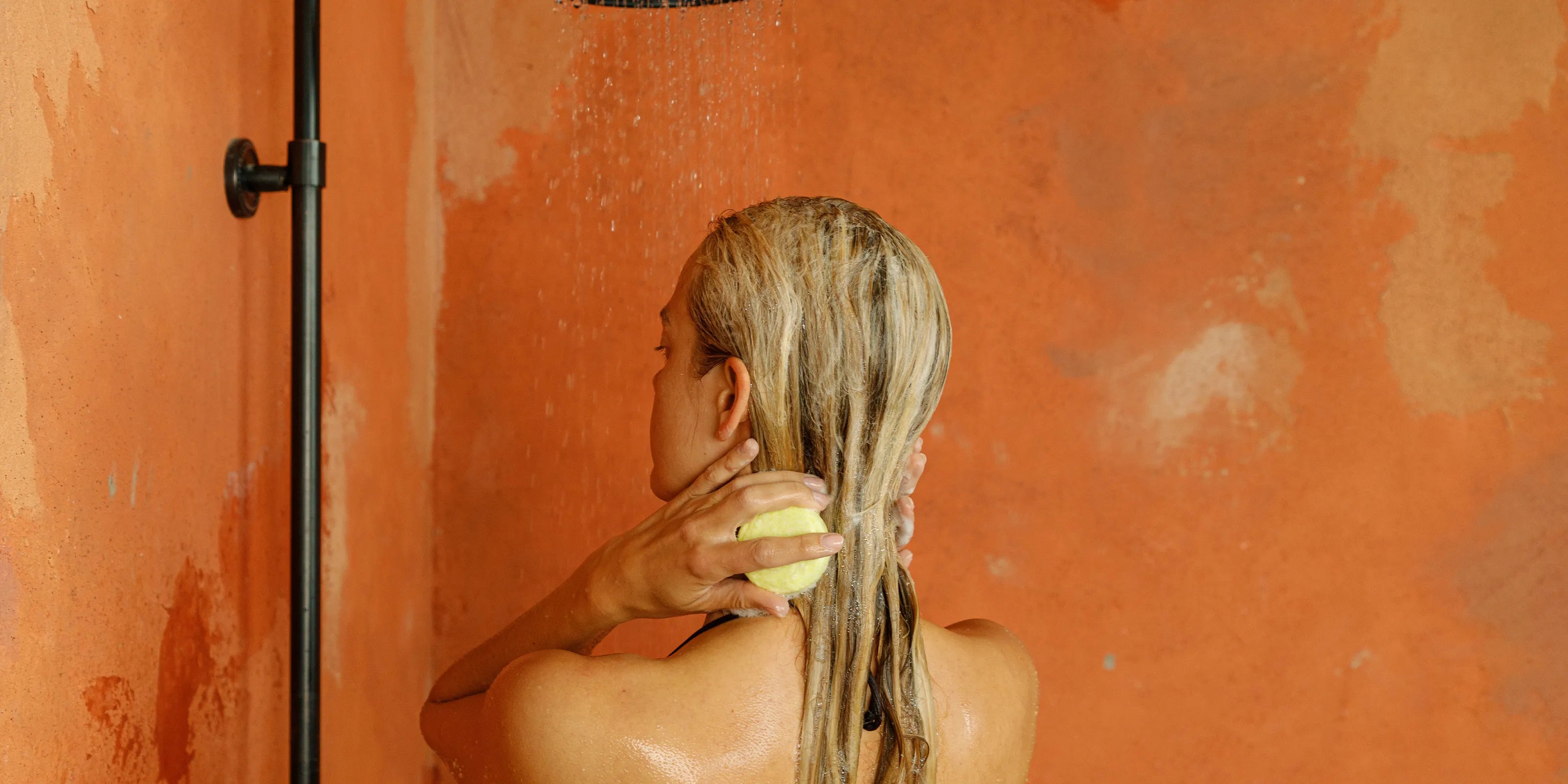 a woman showering with a natural shampoo bar. A banner photo for a blog on ingredients to avoid in shampoo