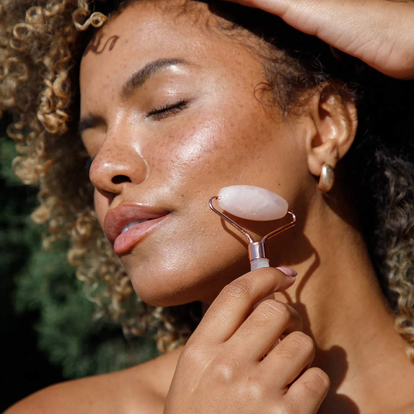 a rose quartz roller on a womans face for a blog photo about jade vs rose quartz rollers