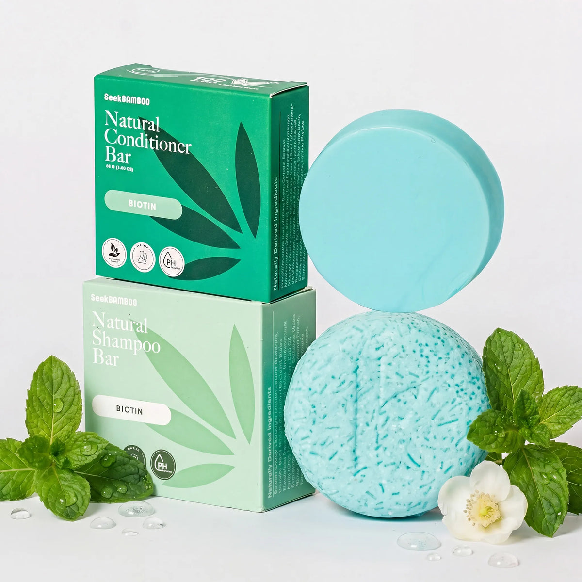 biotin shampoo and conditioner bars and their packaging with mint leaves and a flower on a light background