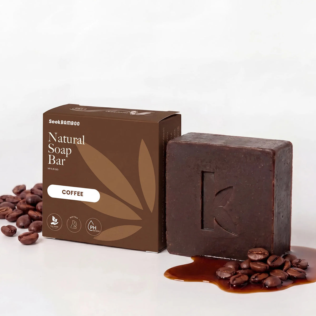 A dark brown coffee soap bar, sits beside its matching brown box on a white background. Styled with scattered coffee beans.