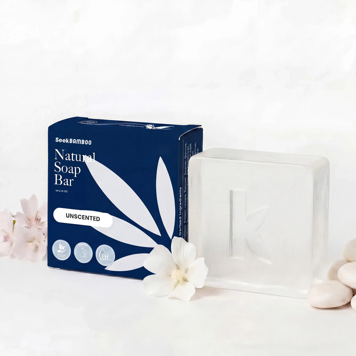 A natural unscented soap bar in a translucent white rectangular block next to its navy blue packaging box, styled with white flowers and smooth stones on a light marble background.