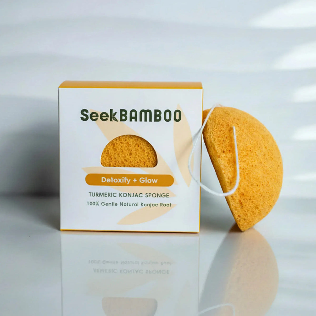 product image for a turmeric konjac facial sponge with one sponge leaning on the branded Seek Bamboo packaging